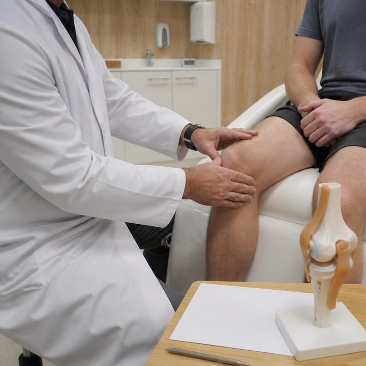 Traumatólogo explorando la rodilla de un paciente para valorar una rotura de menisco